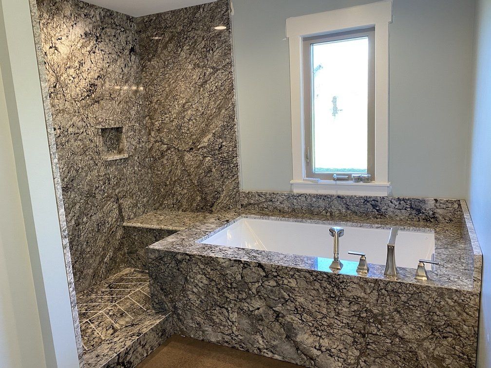 Bathroom with granite walls and tub, shower and window.