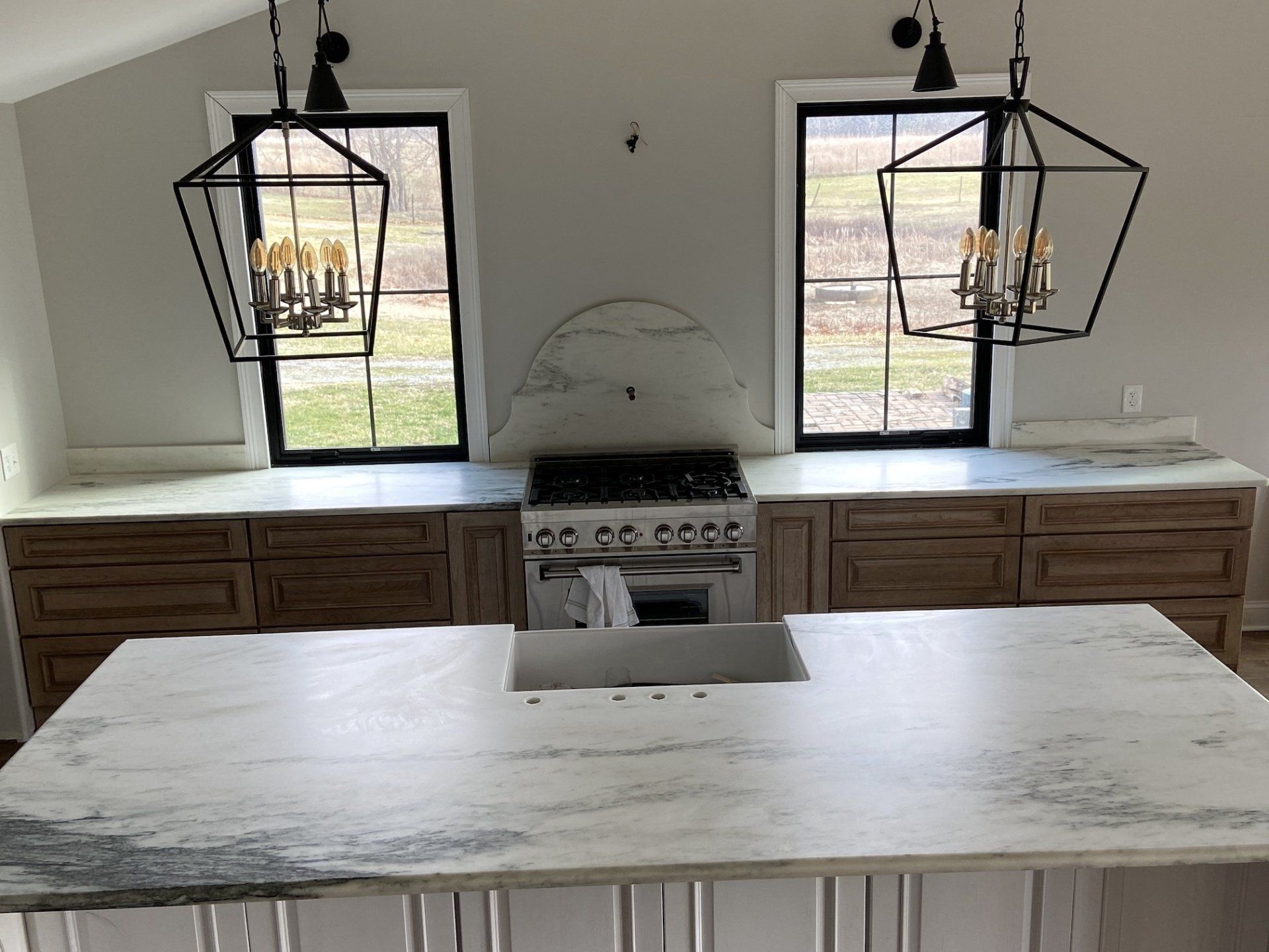 Kitchen with island, stove, windows, and pendant lights. Light countertops, dark cabinets.