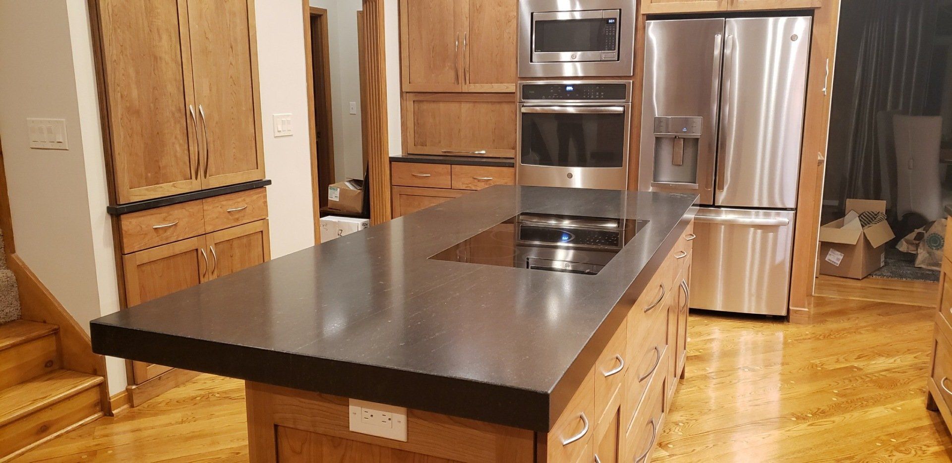 Kitchen with wooden cabinets and island, black countertop, stainless steel appliances, and wood floor.