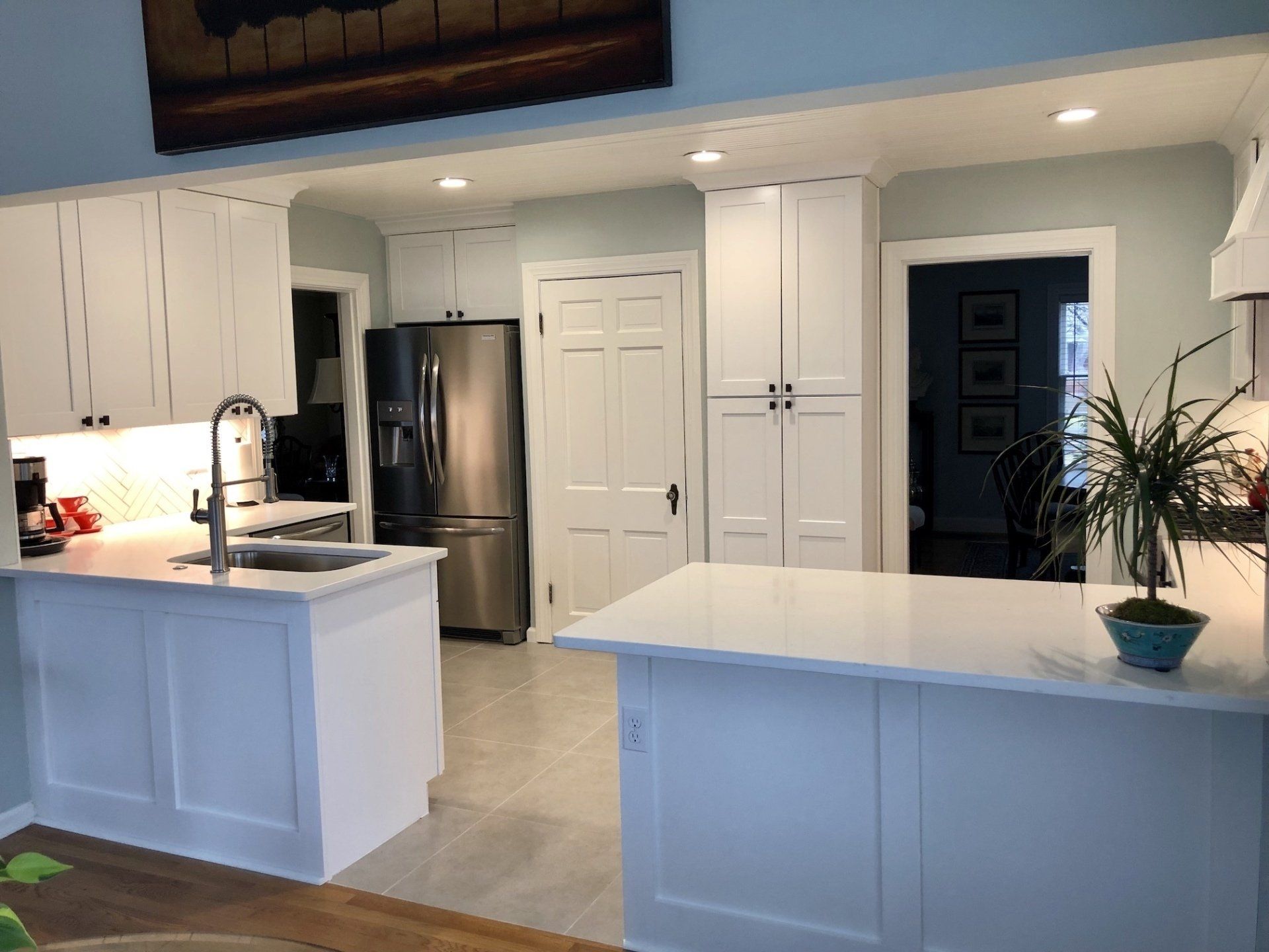 White kitchen with island, cabinets, stainless steel refrigerator, and light blue walls.