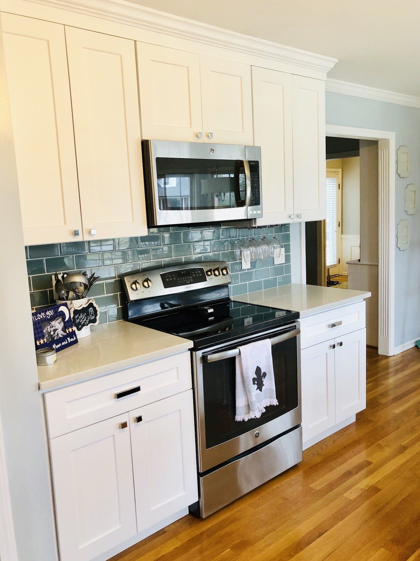 White kitchen with stainless steel stove and microwave, blue tile backsplash, and hardwood floor