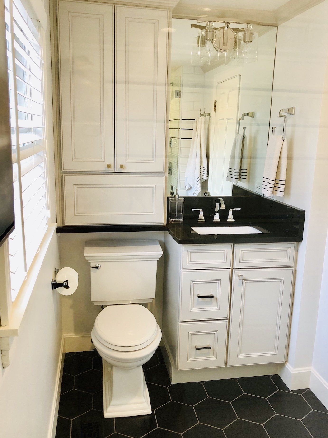 Small white bathroom with black hexagon floor tiles, toilet, sink, and storage cabinets.