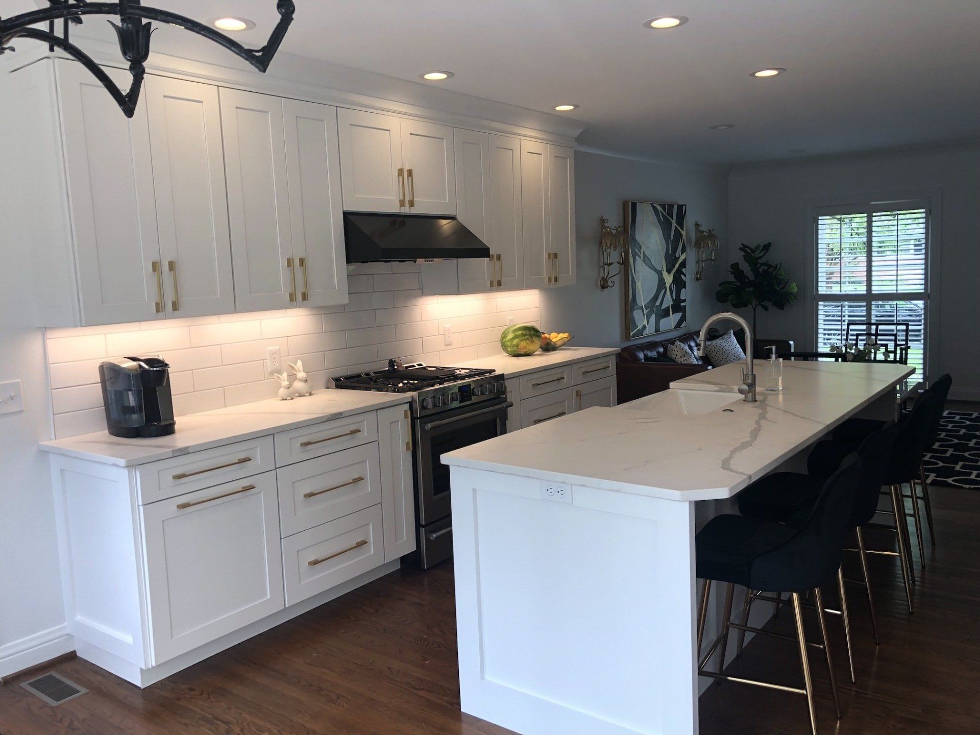 White kitchen with island, quartz countertops, and gold hardware. Black range hood and stools.