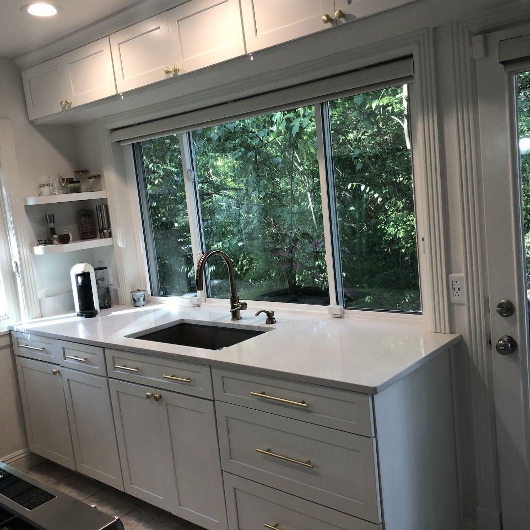 White kitchen with cabinets, sink, window overlooking trees, and a door.