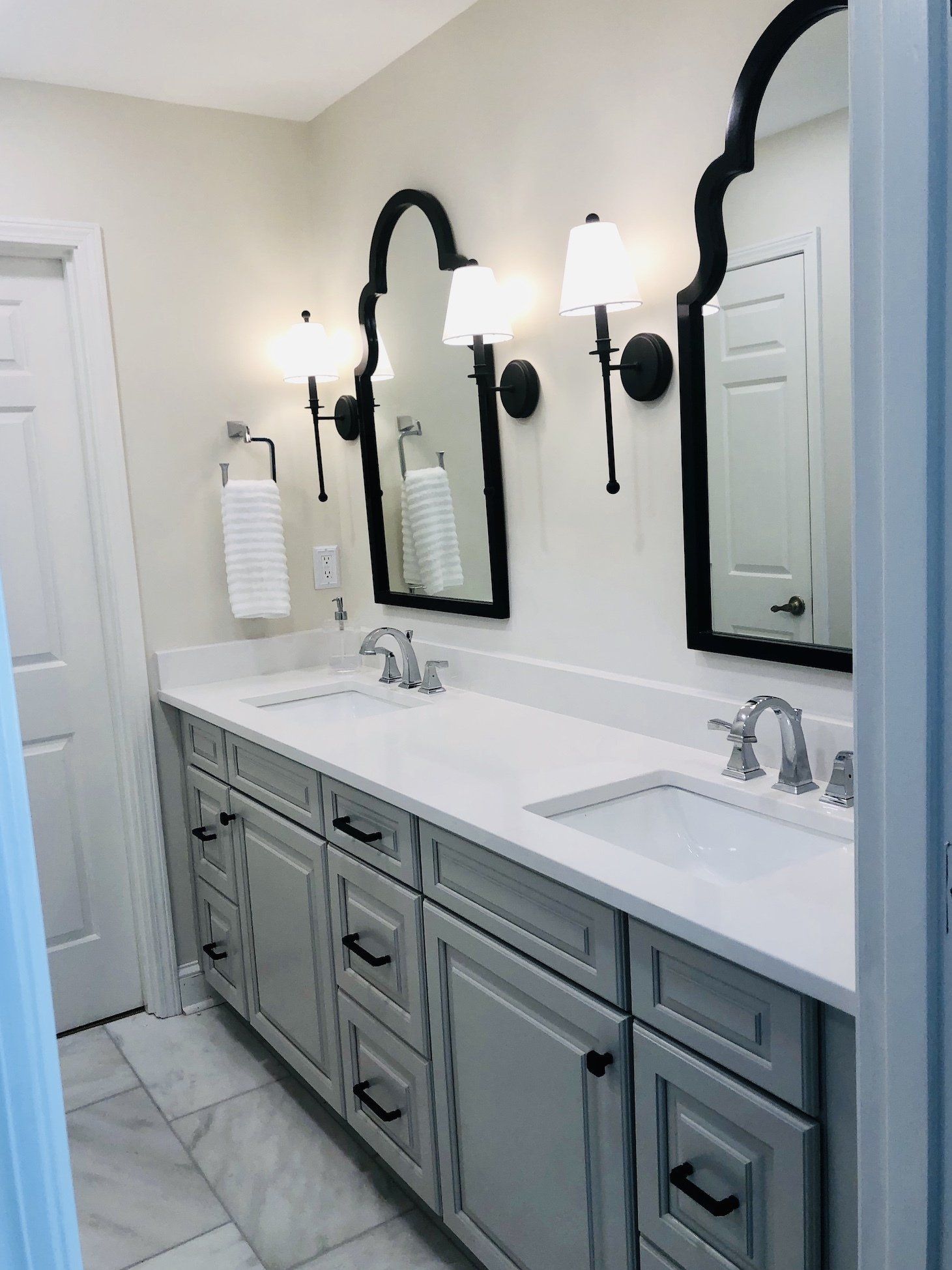 Bright bathroom vanity with two sinks, gray cabinets, and black arched mirrors and sconces