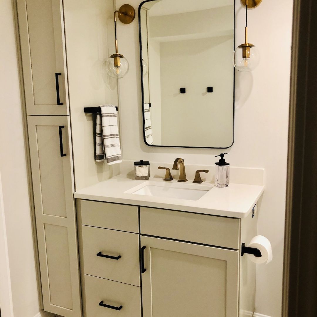 Bathroom with white cabinets, gold fixtures, and a black-framed mirror.