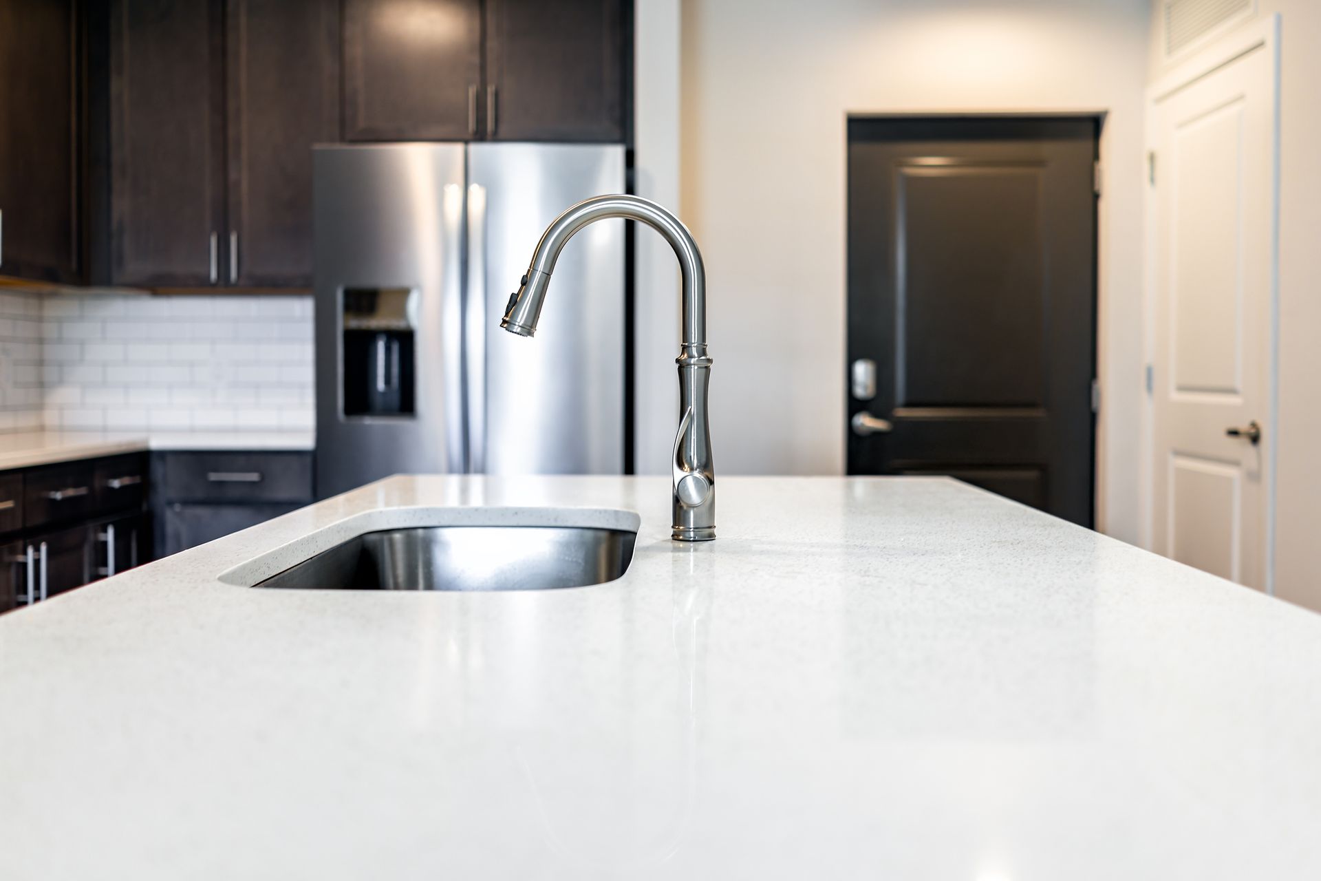 Modern kitchen with white island countertop, stainless sink, chrome faucet, and dark cabinets