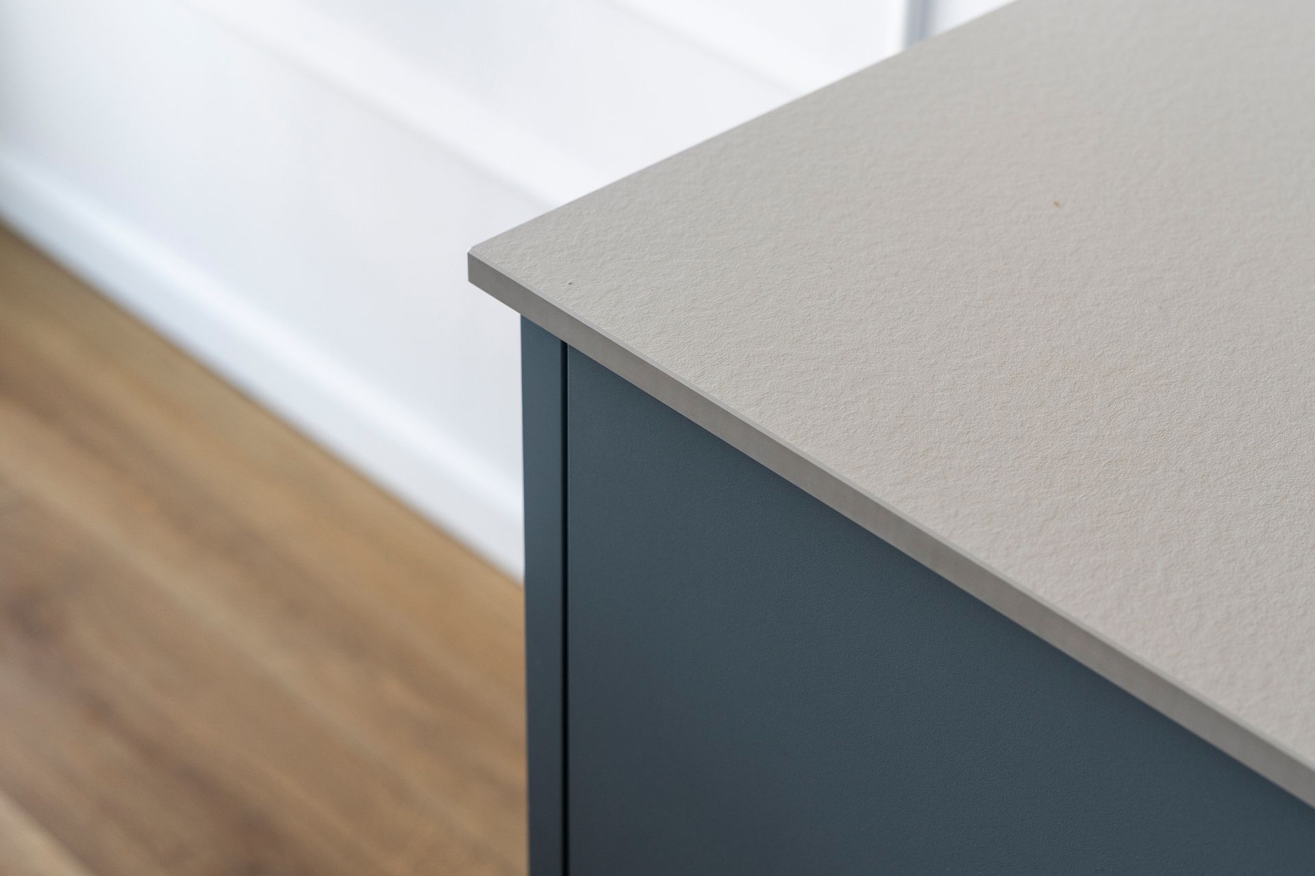 Close-up of a blue cabinet with a light gray textured countertop. Wooden floor and white wall in background.
