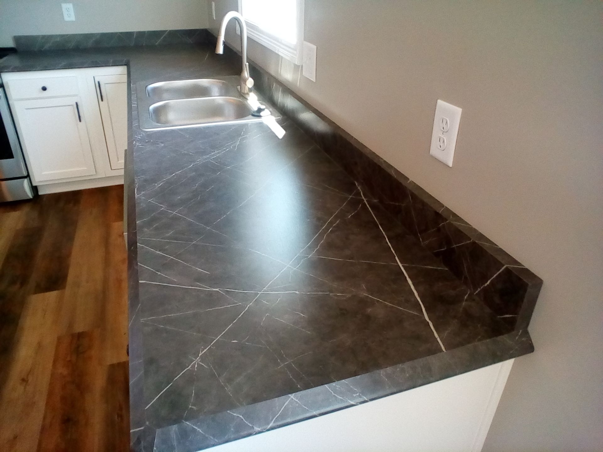 Dark gray countertop with a white veining pattern; kitchen sink; white cabinets.