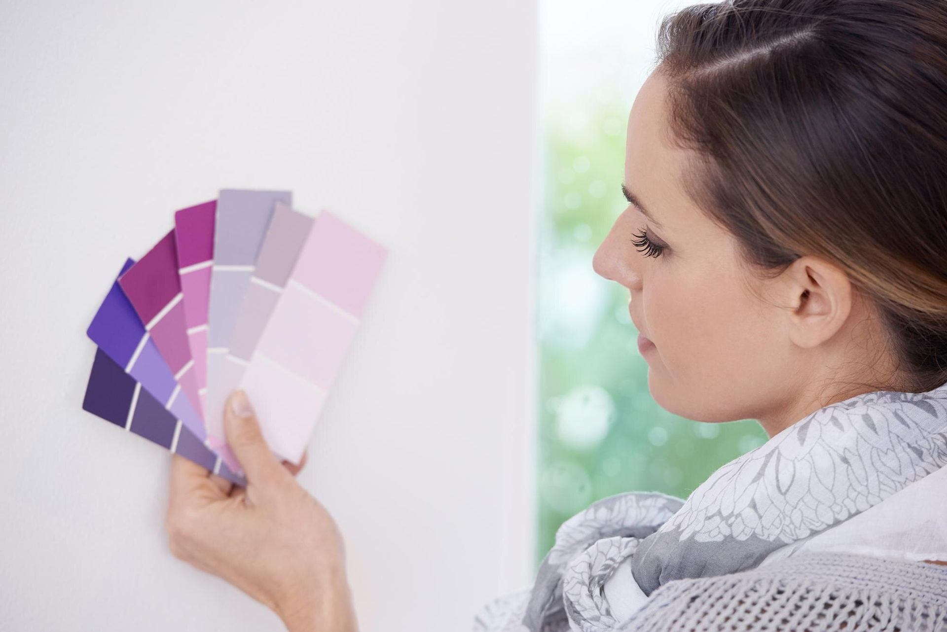 woman looks at purple colour swatches against white wall