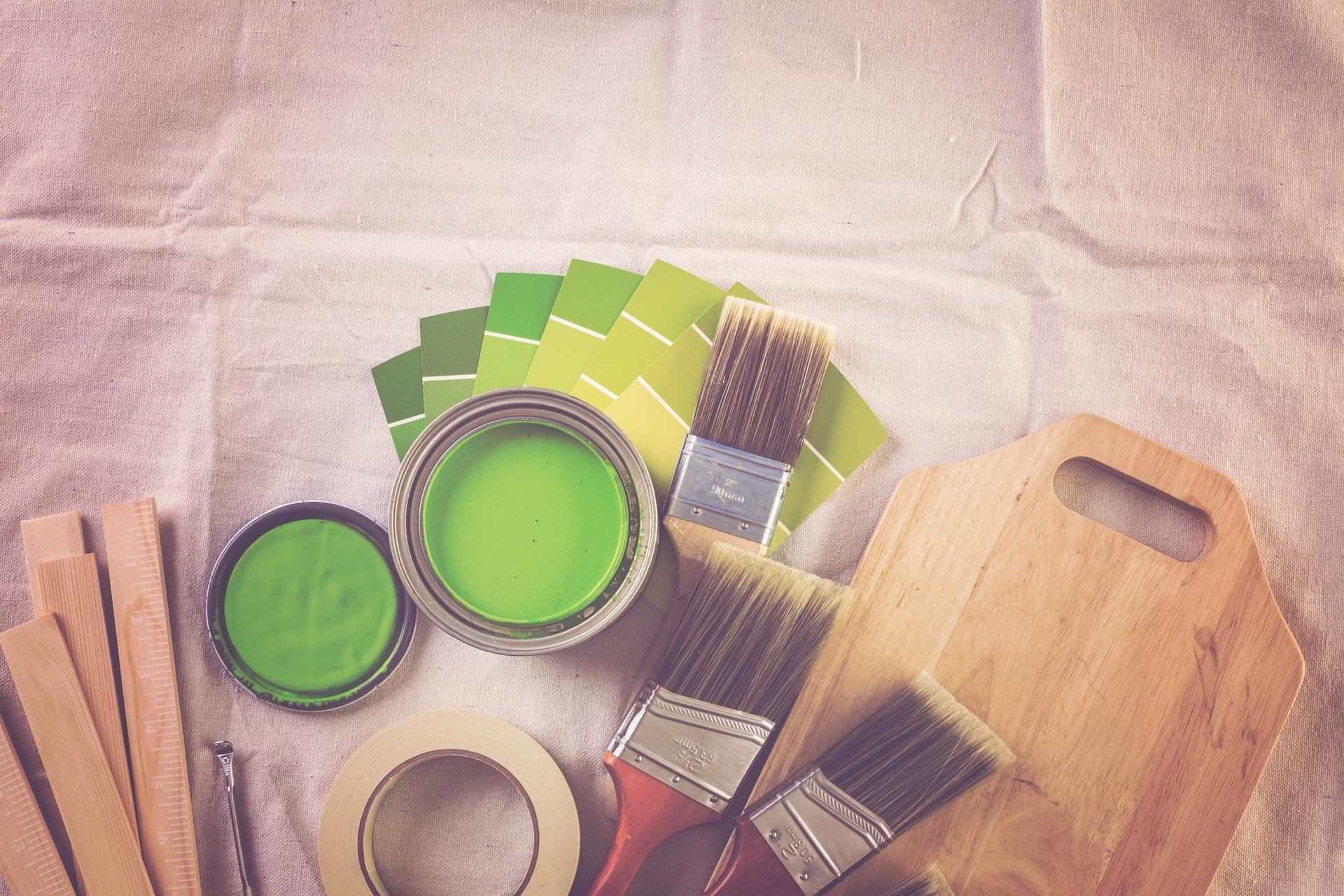 Green paint, paintbrushes, colour swatches, and tape on a white cloth.