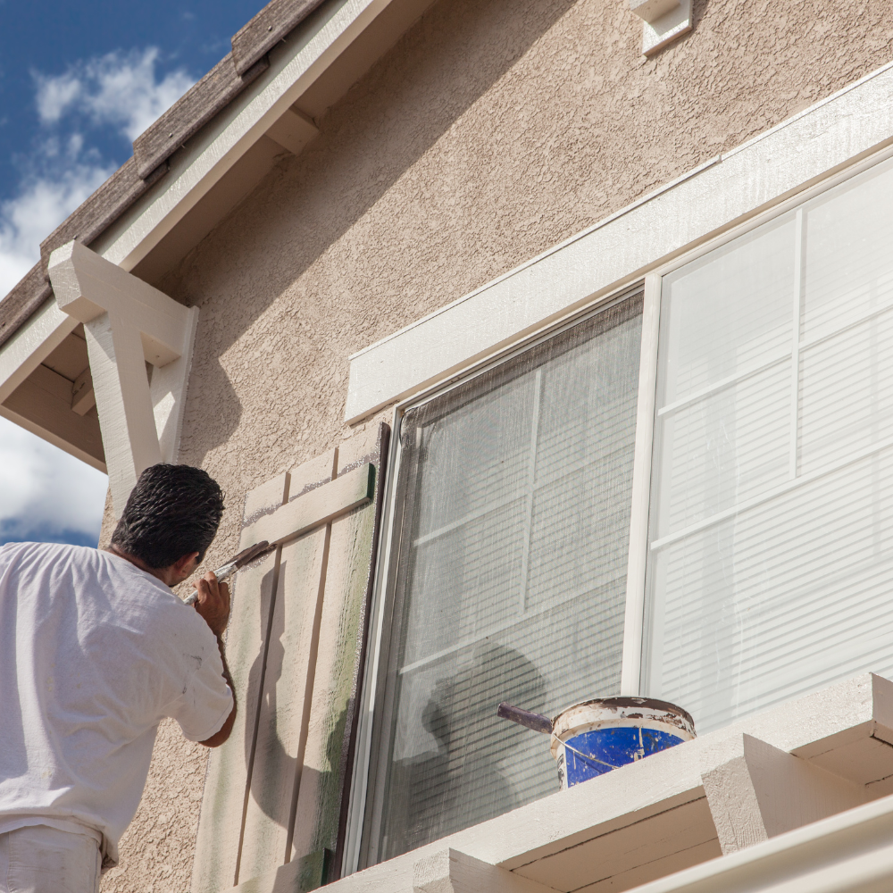 professional painter applying paint to a windows shutters from the outside.