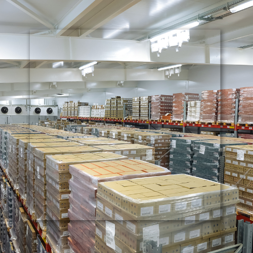 Boxes stacked high in a refrigerated warehouse, with industrial shelving and overhead lighting.