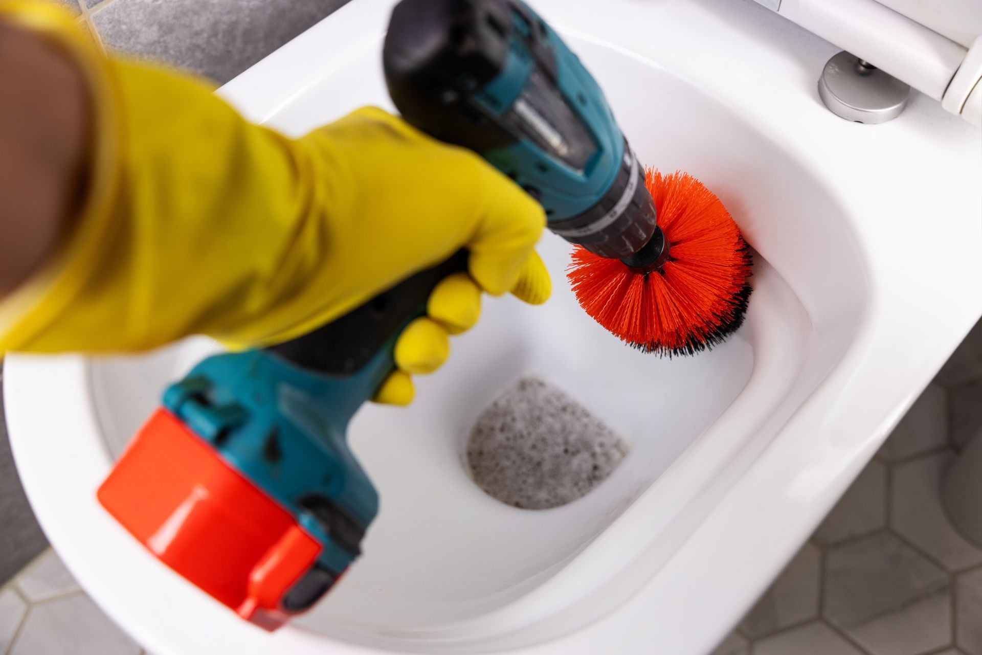 Person cleaning a white toilet with a blue-and-black scrub brush and yellow gloves