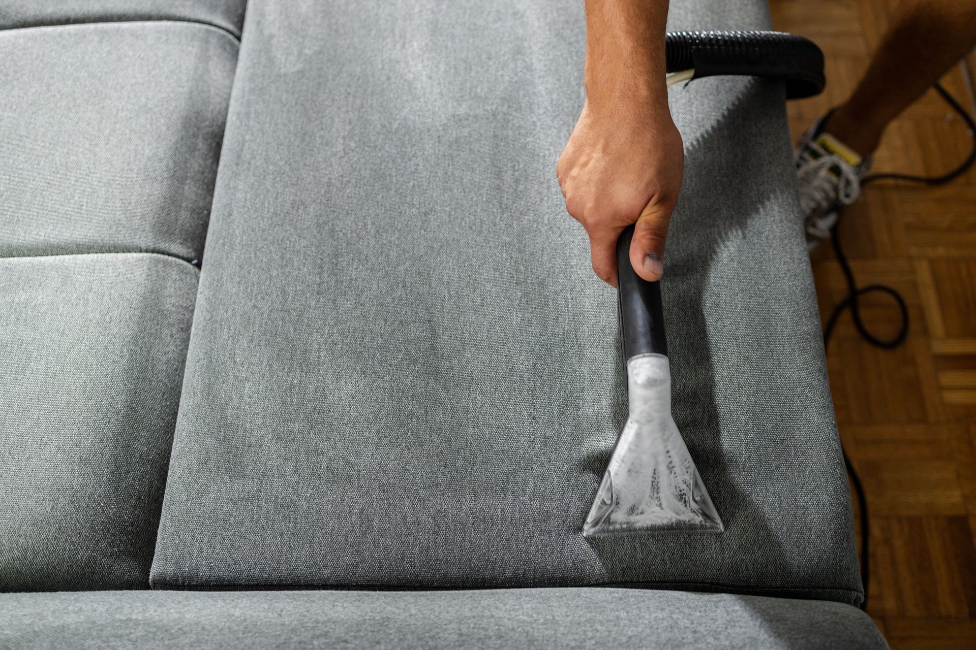 Person using a handheld upholstery cleaner on a gray sofa cushion