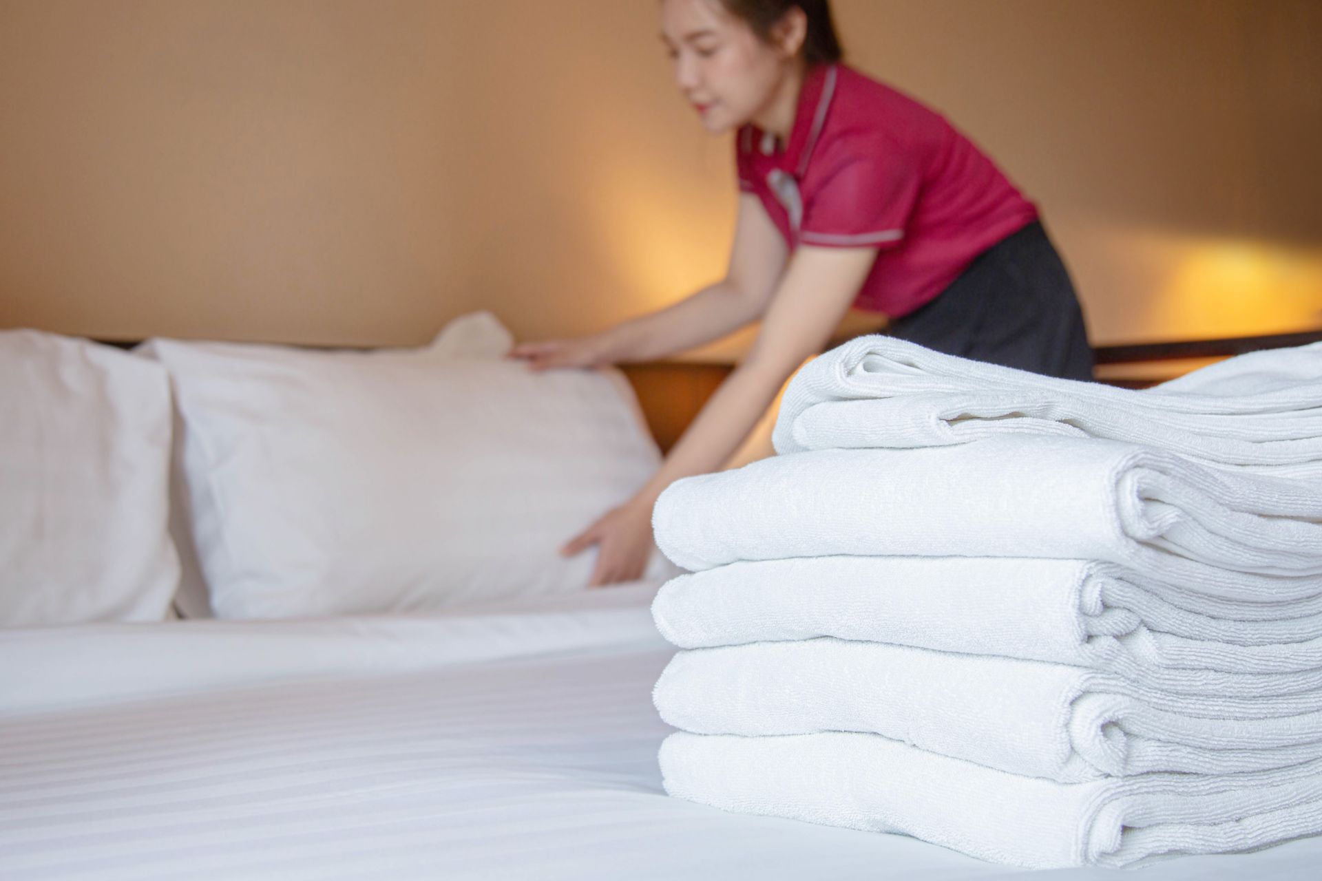 Housekeeper making a bed with neatly folded white towels in a warm-lit bedroom