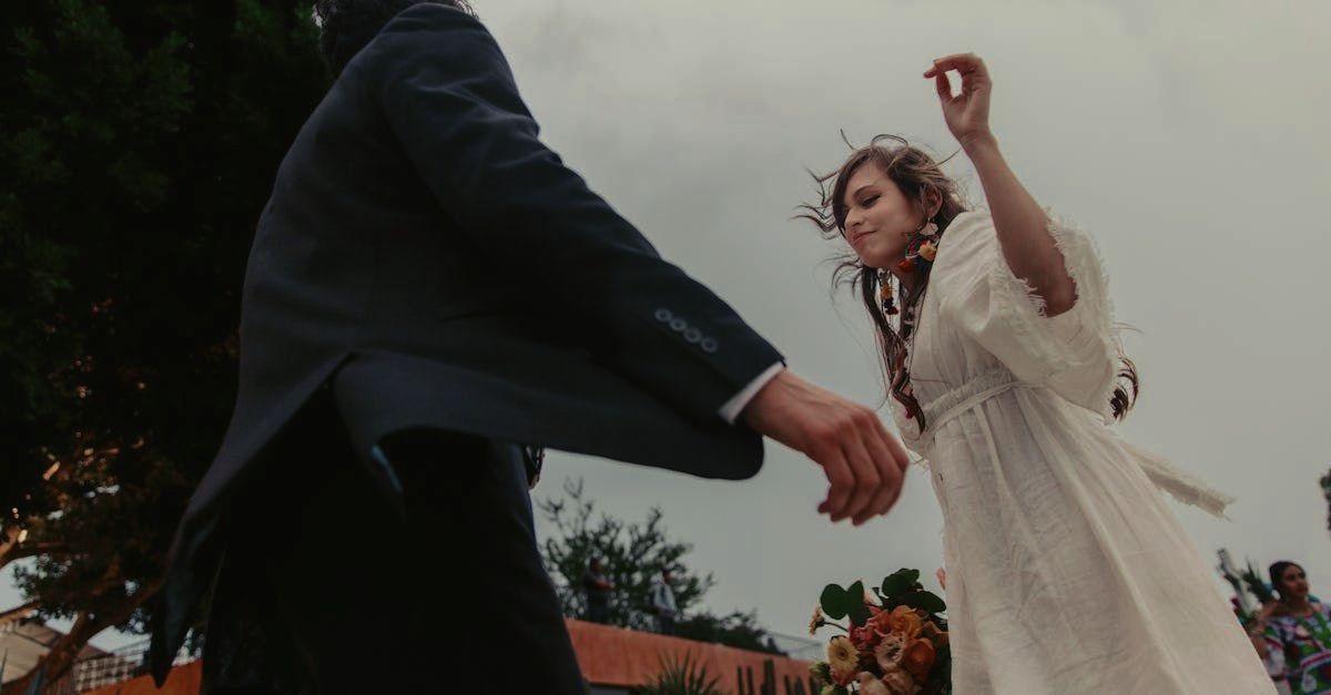 Un homme en costume tient la main d'une femme en robe blanche.