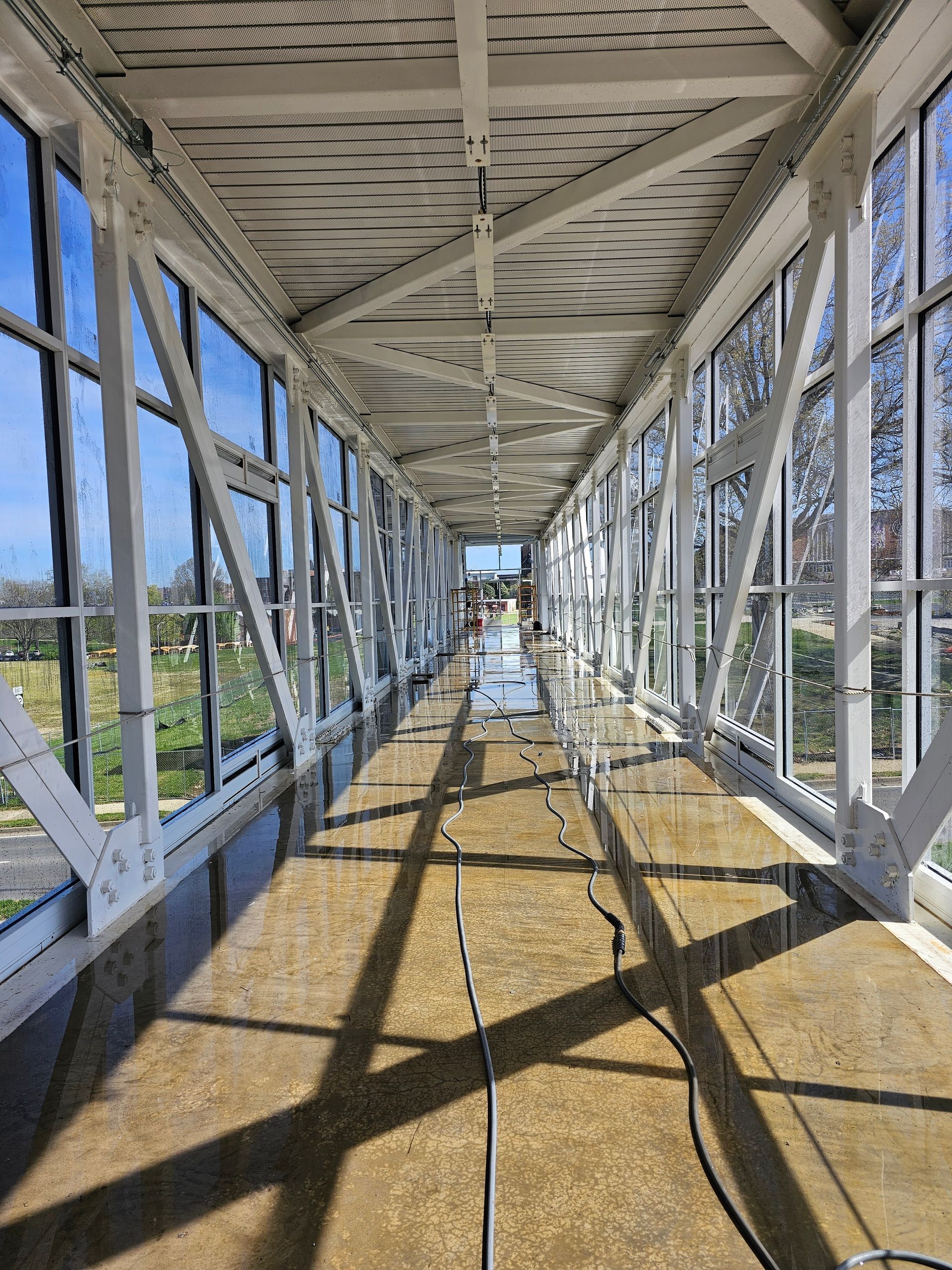 Covered pedestrian bridge interior with white metal trusses and sunlight casting shadows on the floor
