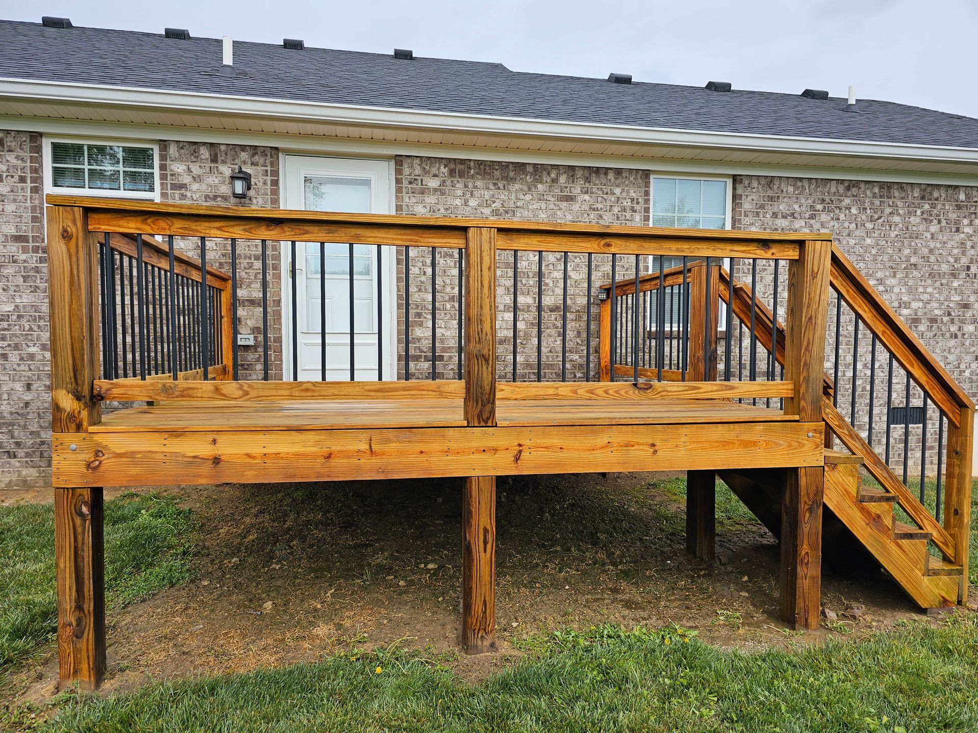 Wooden raised deck with railings and stairs beside a brick house
