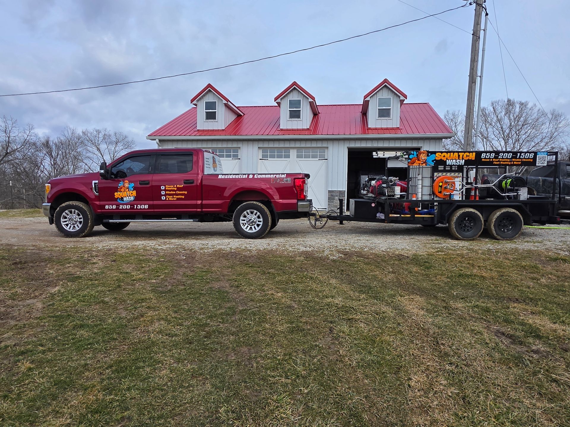 Red tow truck with equipment trailer parked beside a small white building with red roof and dormers.