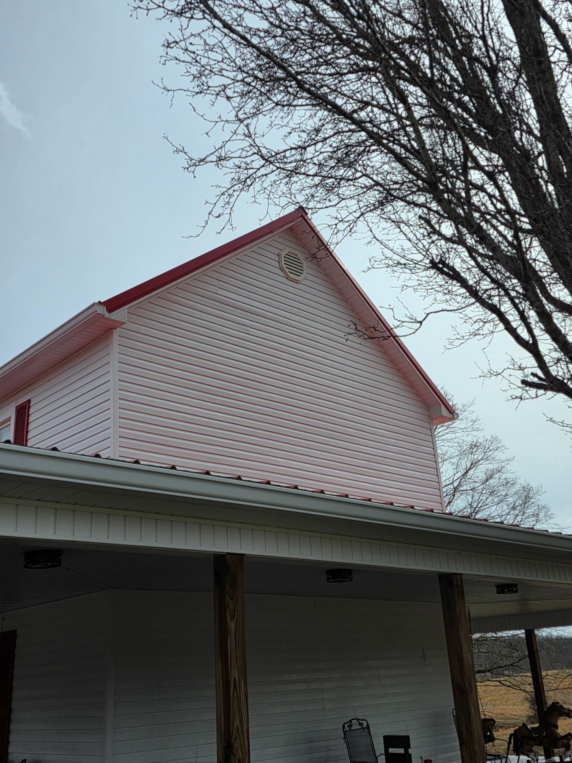 White barn with red roof and white siding under bare tree branches on an overcast day