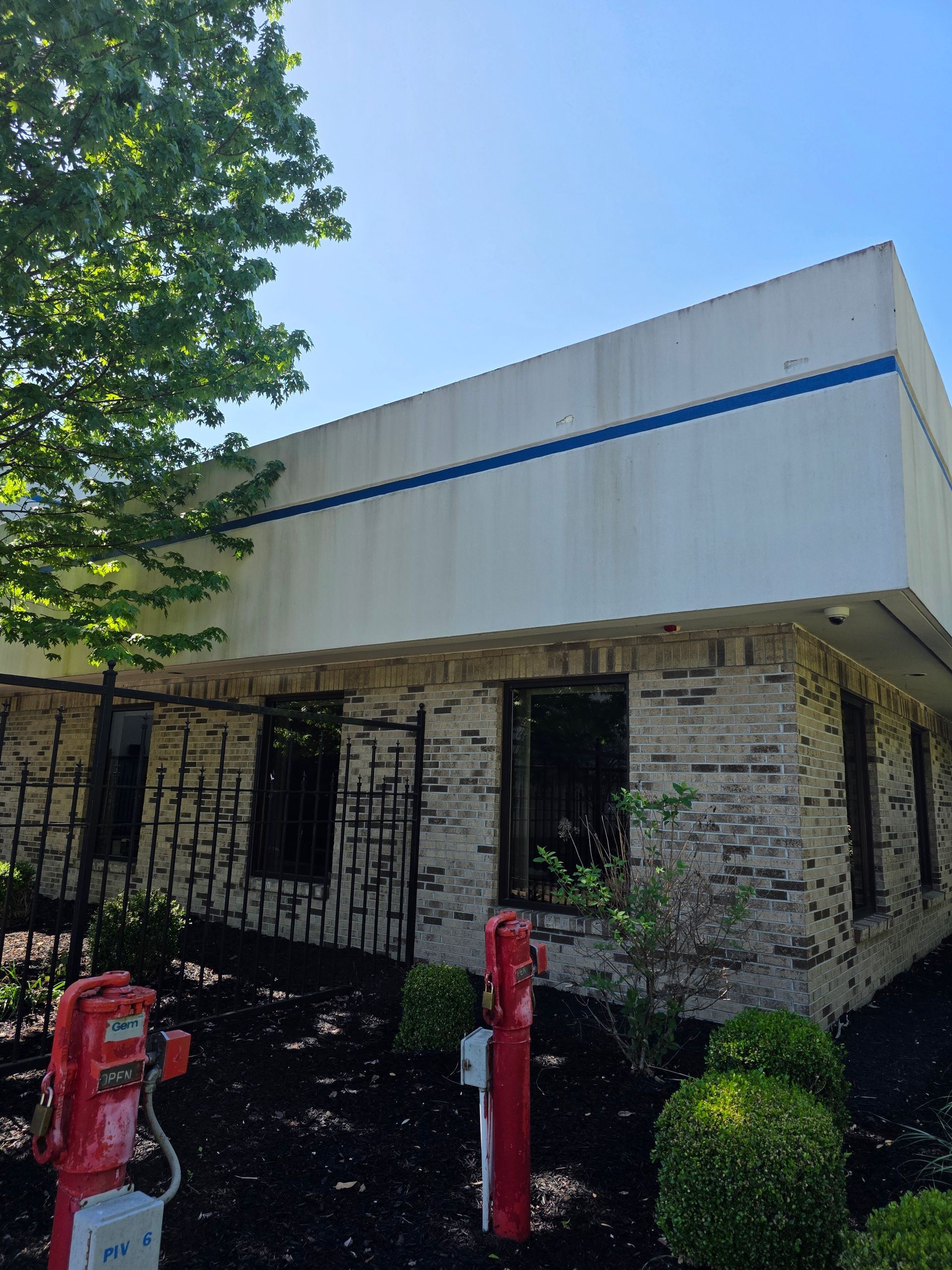 Small stone building with white awning, blue trim, red posts, and a tree casting shade.