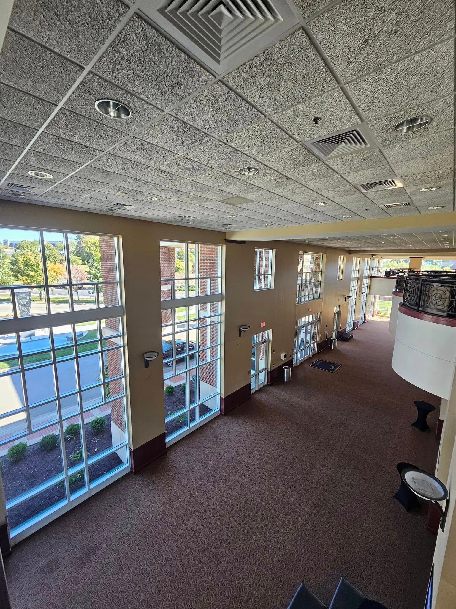Bright gym interior with treadmills, large windows, carpeted floor, and a drop ceiling