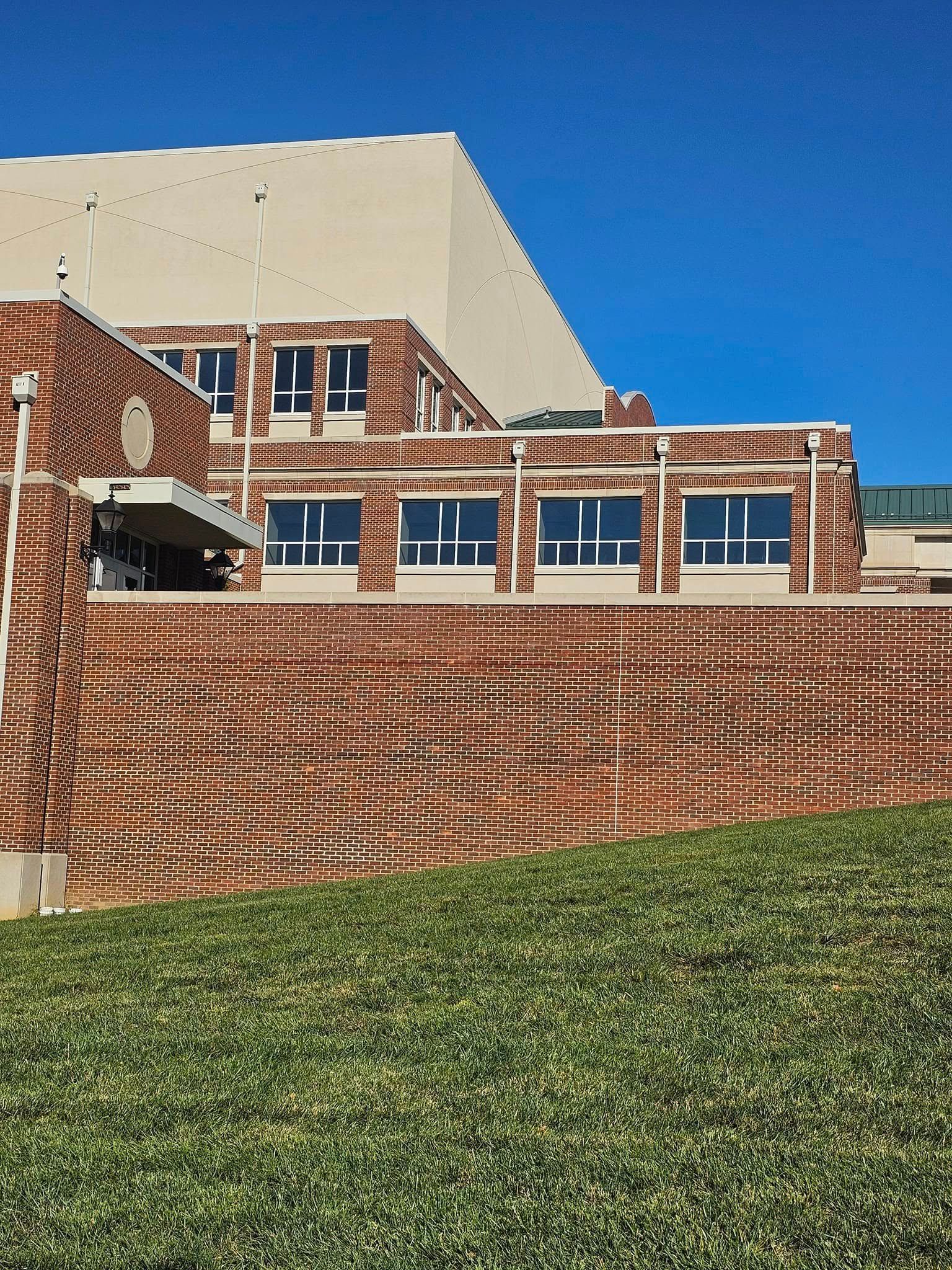 Brick building with large windows behind a sloped terraced lawn under a clear blue sky