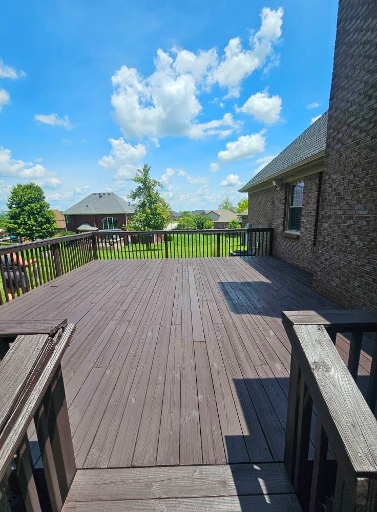 Wooden deck with railings beside a brick house under a bright blue sky and clouds