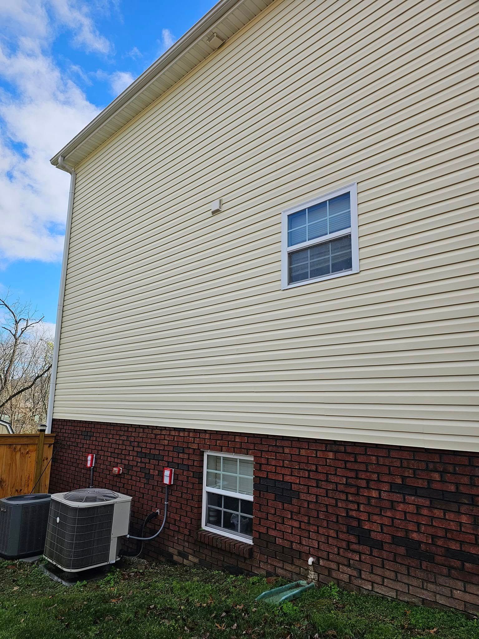 House exterior with cream siding over red brick, a window, and an outdoor HVAC unit beneath a blue sky
