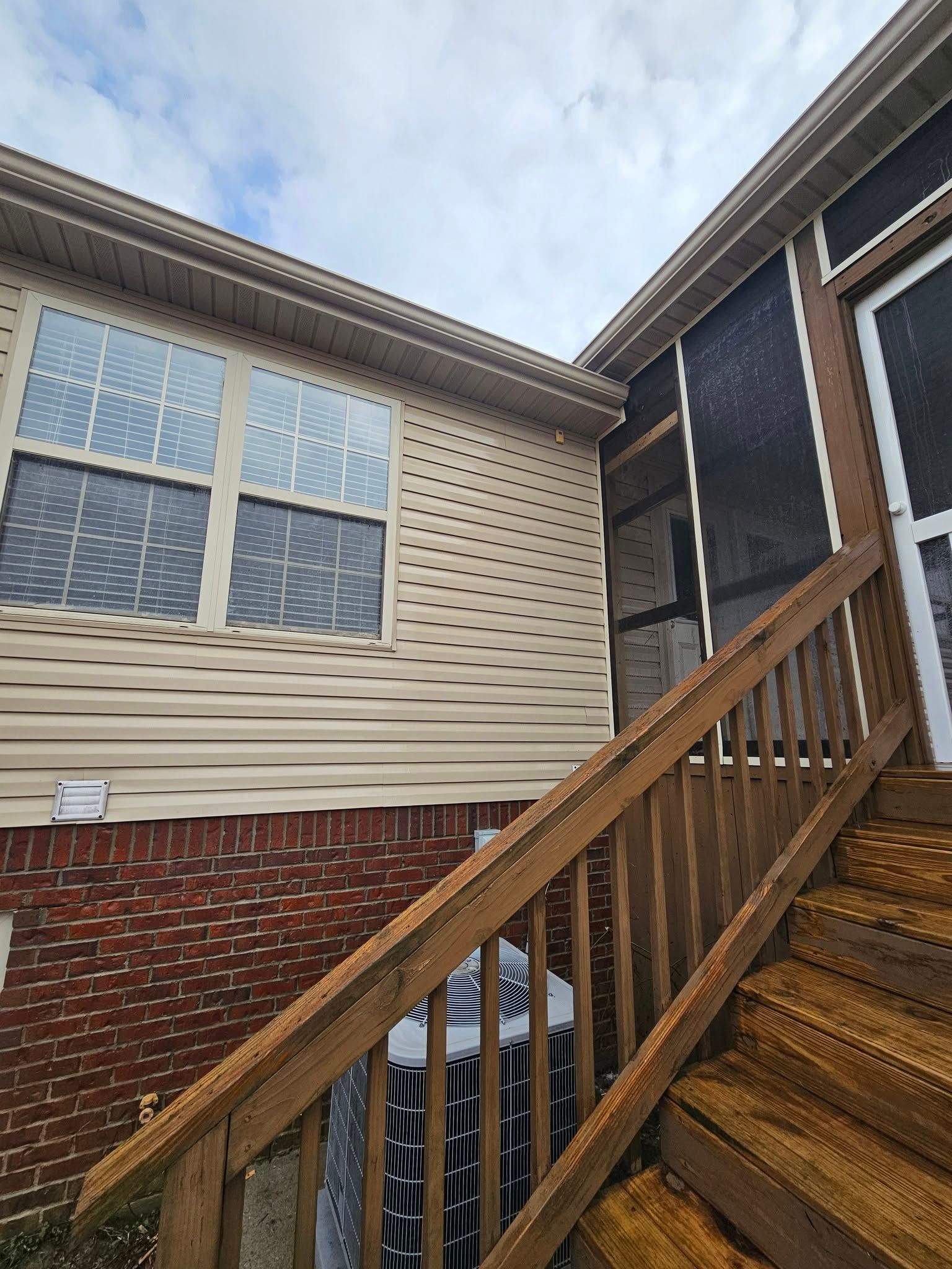 Exterior stairway beside a beige and brick house under a cloudy sky