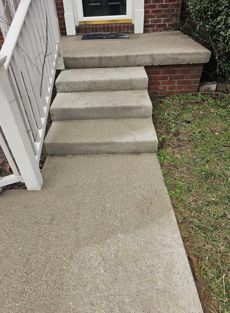 Concrete front steps leading to a brick house entrance beside a white railing.