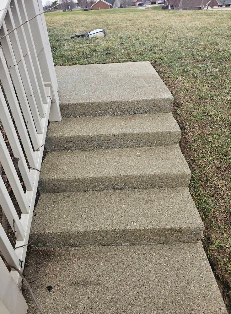 Concrete steps leading to a grassy yard beside a white railing and house exterior.
