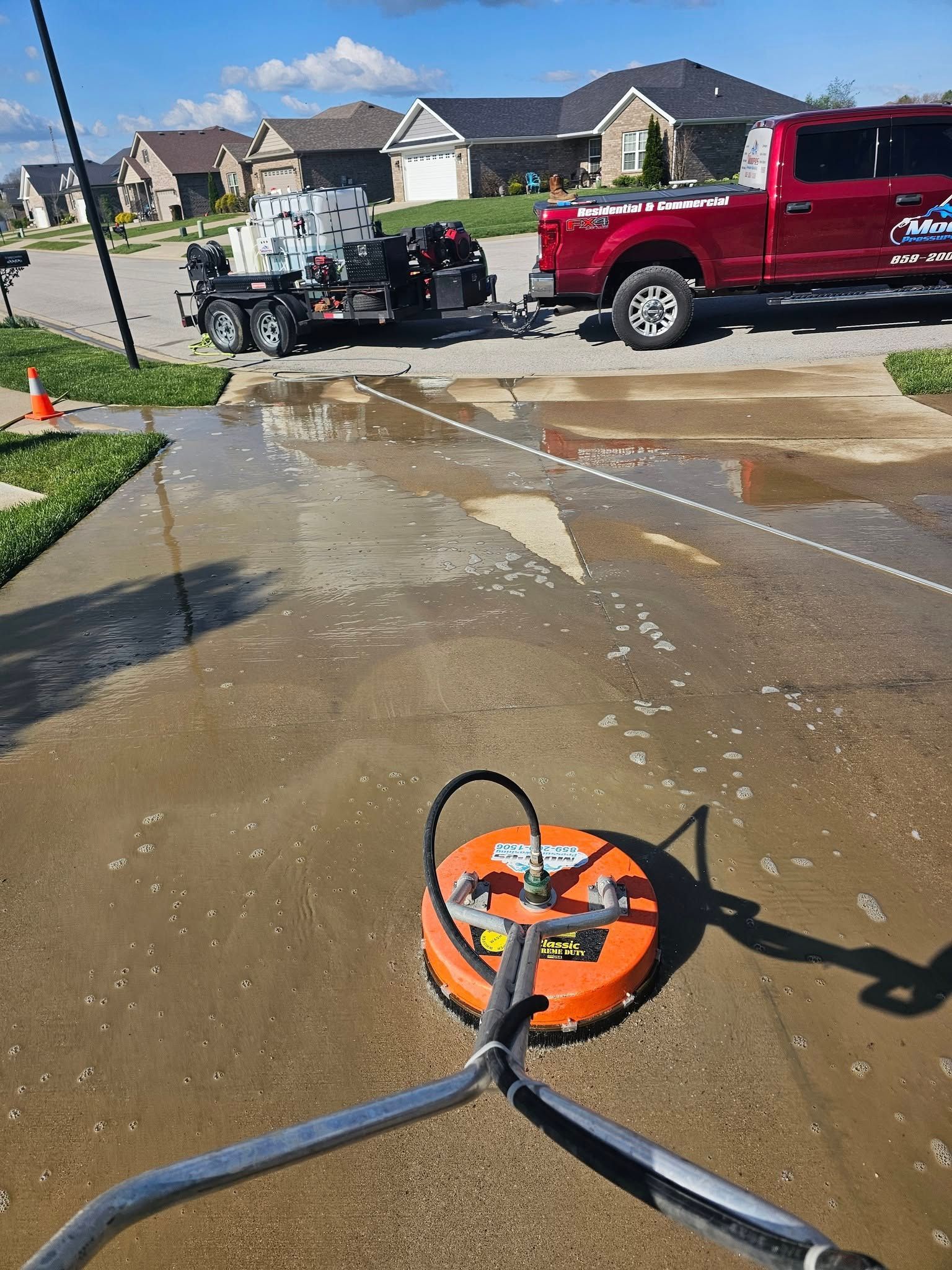 Orange sewer drain cleaner on wet driveway with red pickup truck and flooded street in suburban neighborhood