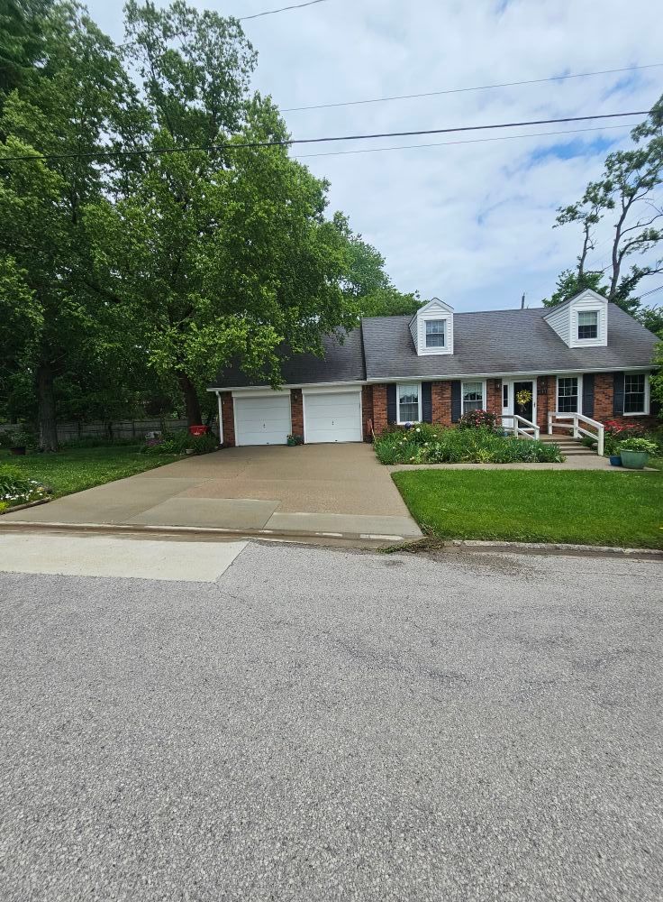 Brick house with two-car garage, wide driveway, and green trees in front yard