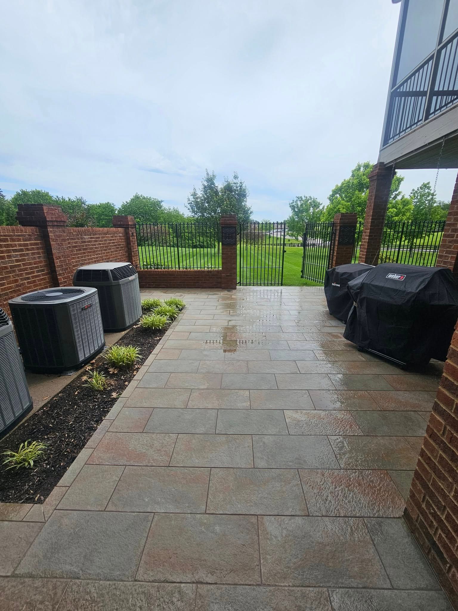 Wet stone patio leading to a wooden gate, with garden fencing and outdoor storage bins on either side.