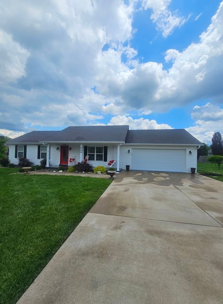 Single-story suburban house with white siding, gray roof, and two-car garage under a partly cloudy sky.