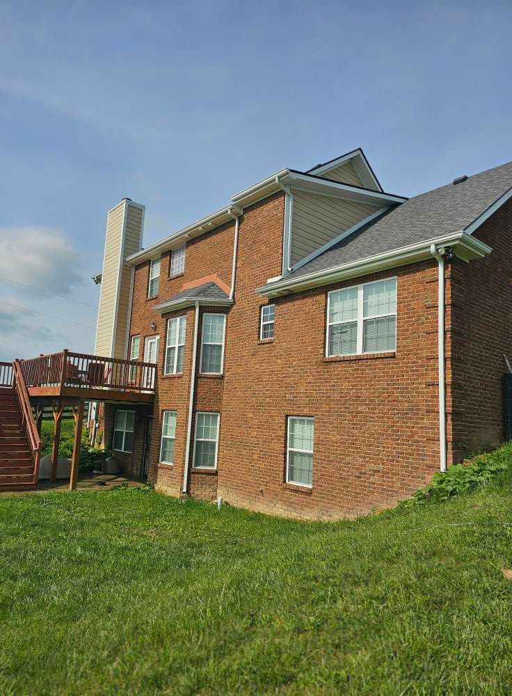Brick apartment building with a wooden balcony and grassy yard under a blue sky