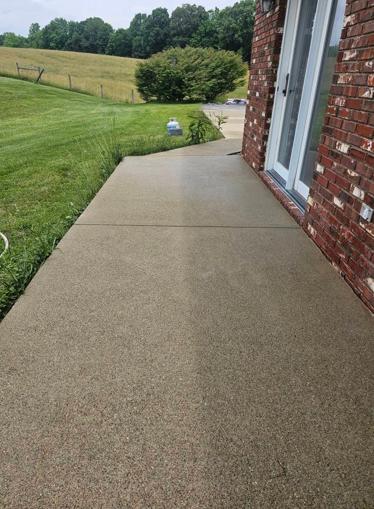 Concrete patio beside brick house overlooking grassy yard and hills