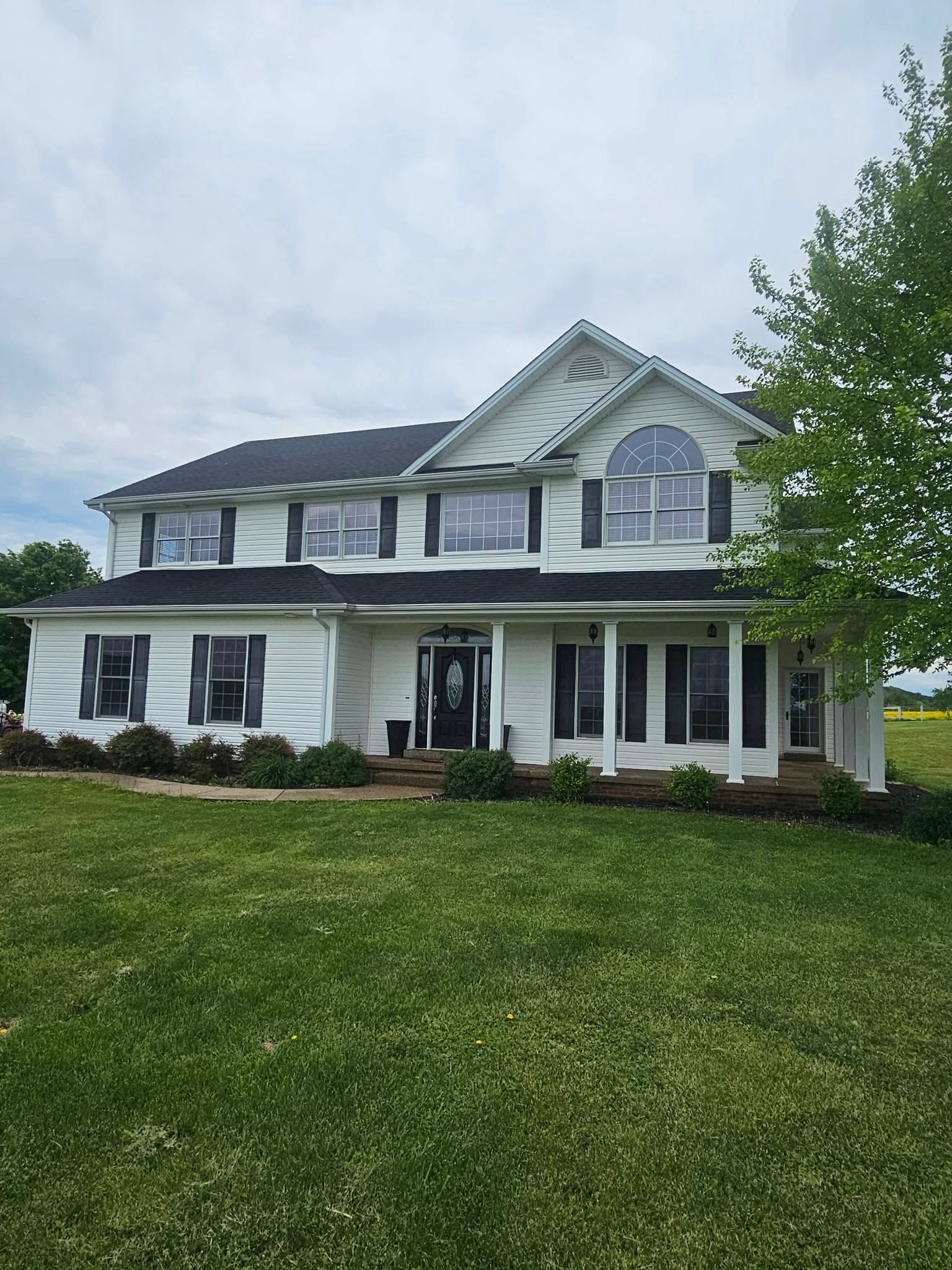Two-story white house with black shutters and a large front lawn under a cloudy sky
