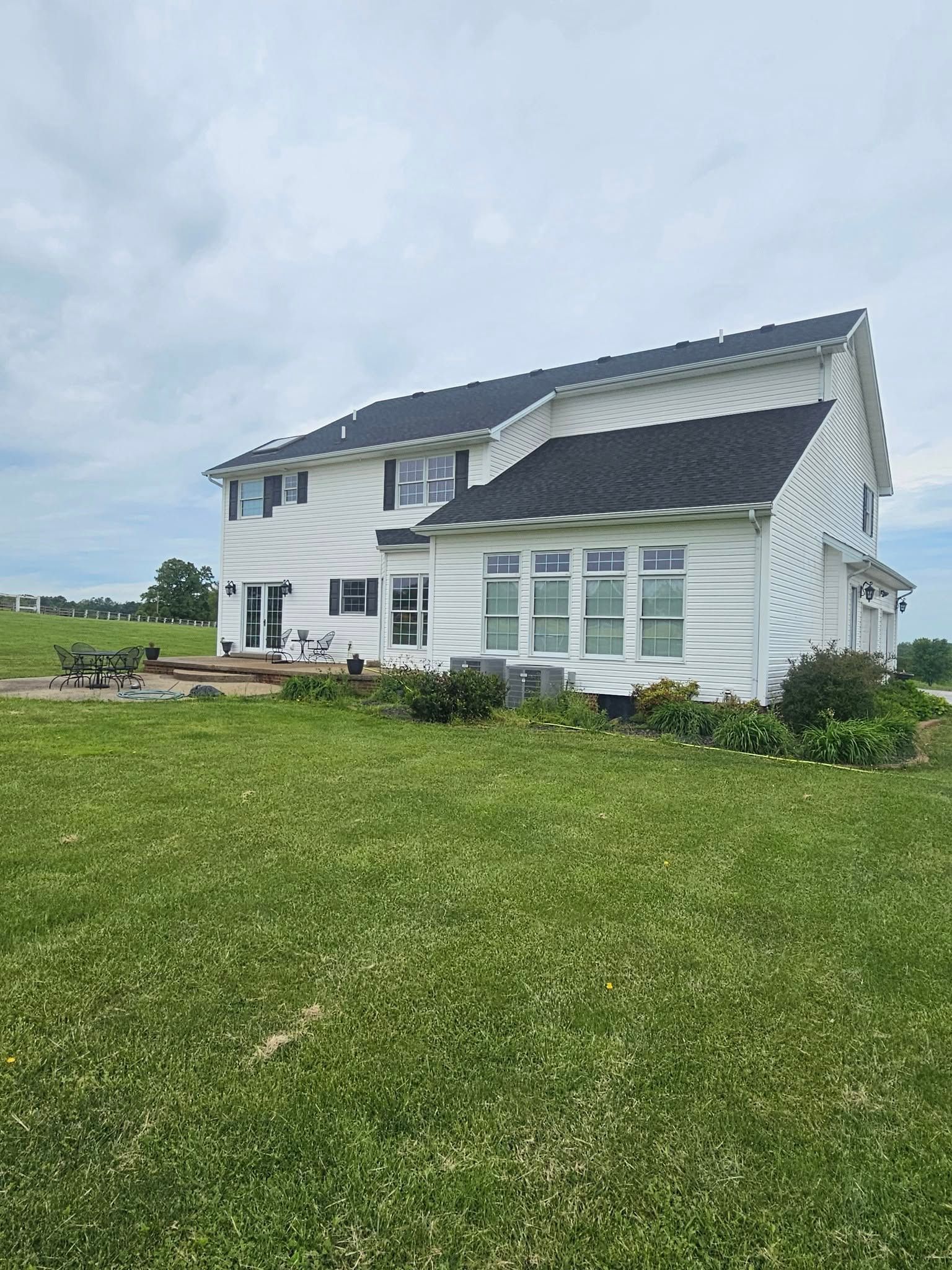 Damaged white two-story house with missing roof panels, surrounded by a grassy field under a cloudy sky