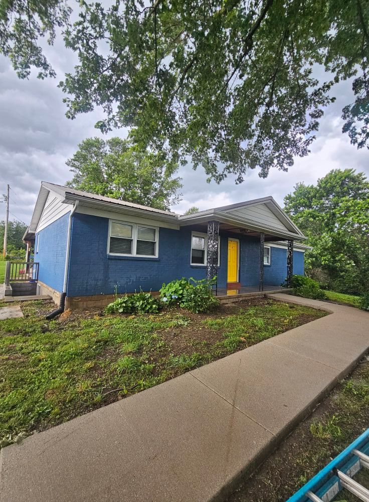 Blue house with yellow door and front walkway under trees on an overcast day
