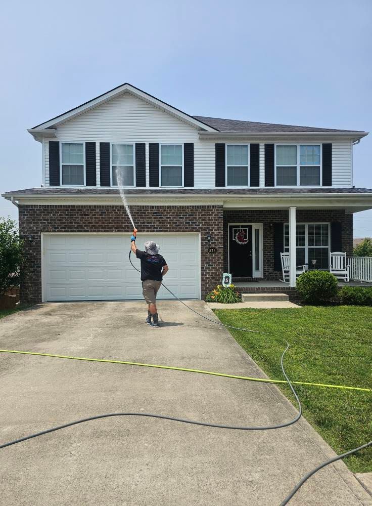 Person standing in driveway outside a two-story house, holding a long pole near the garage.