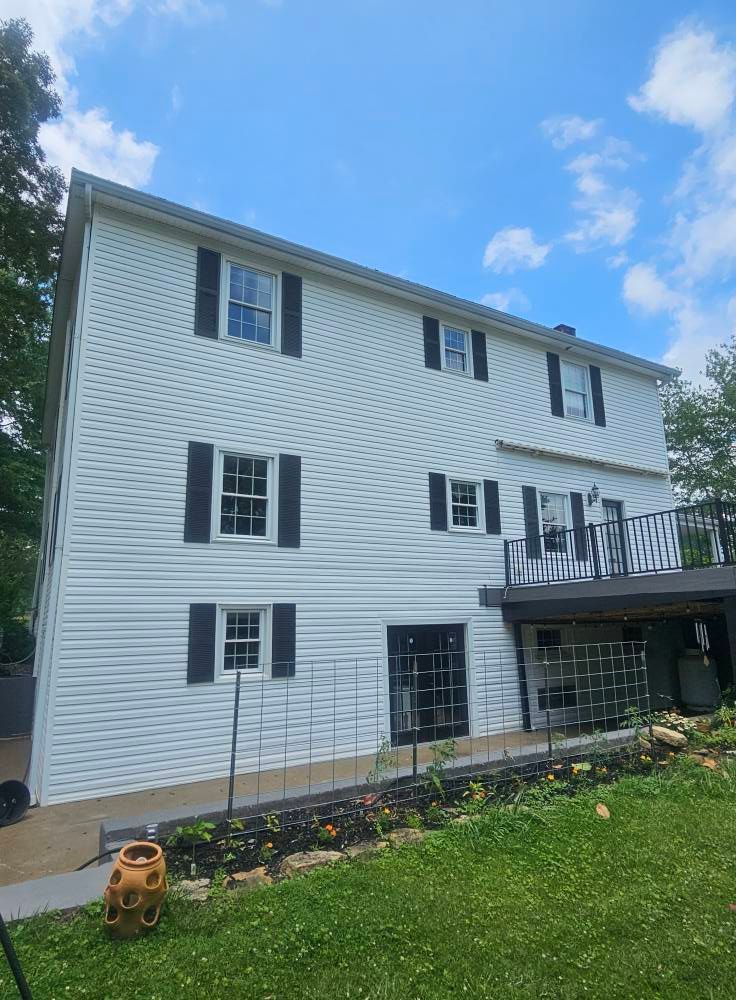 White three-story house with black shutters and a small balcony under a blue sky.