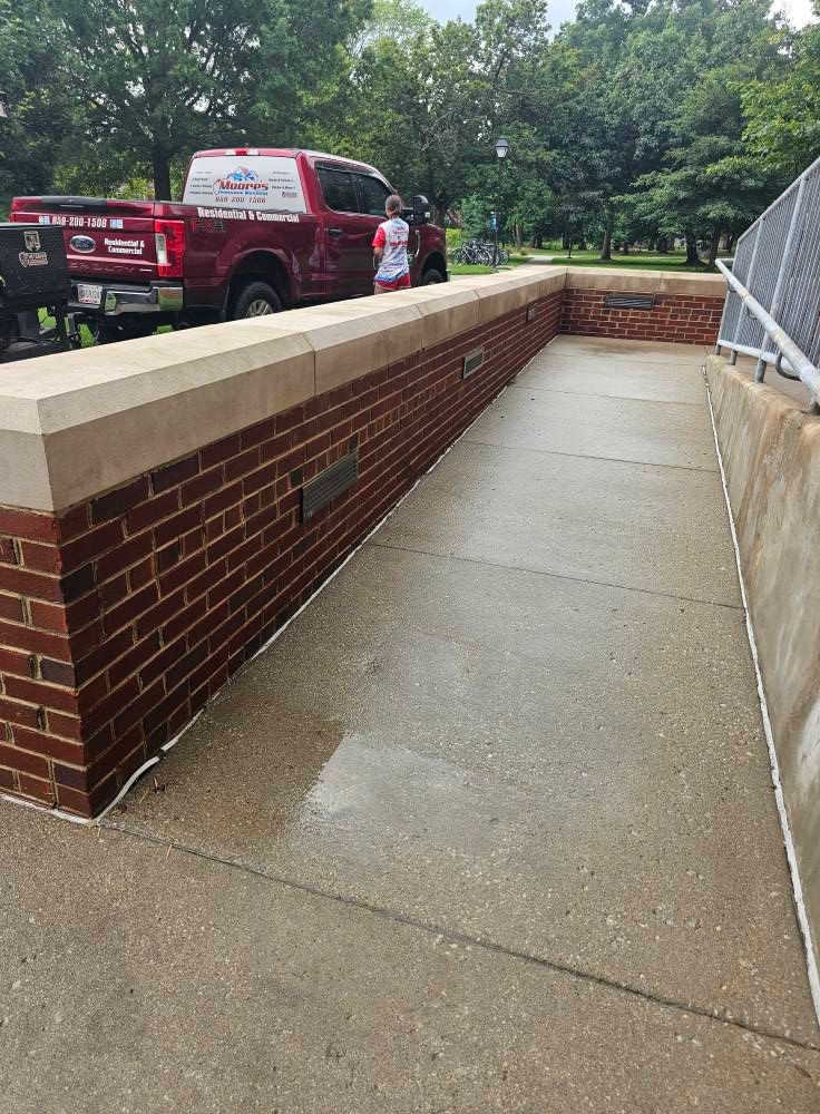 Wet concrete walkway beside a brick wall, with emergency vehicles and trees in the background.