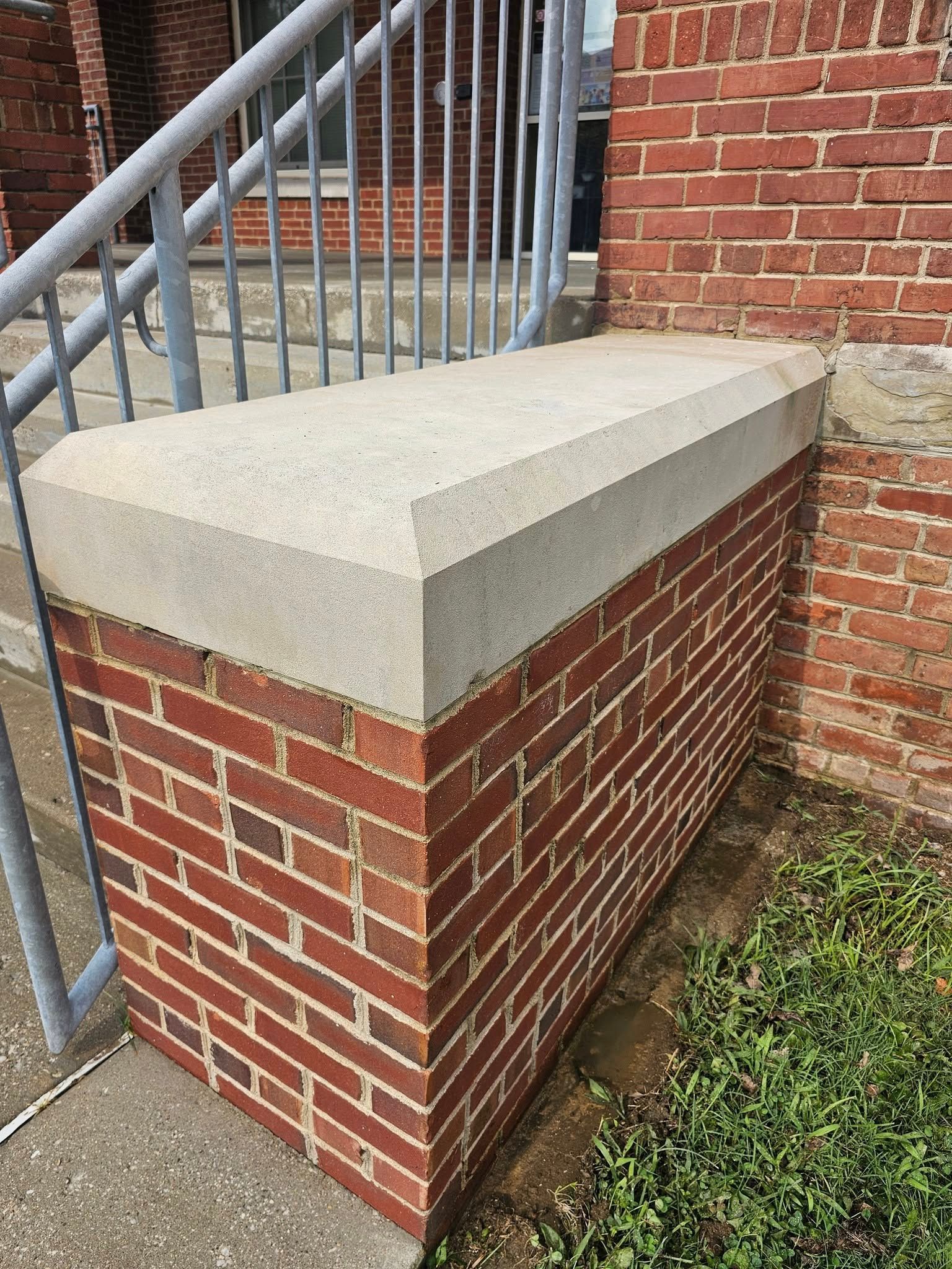 Brick stair landing with a light stone cap beside metal railings and a brick wall