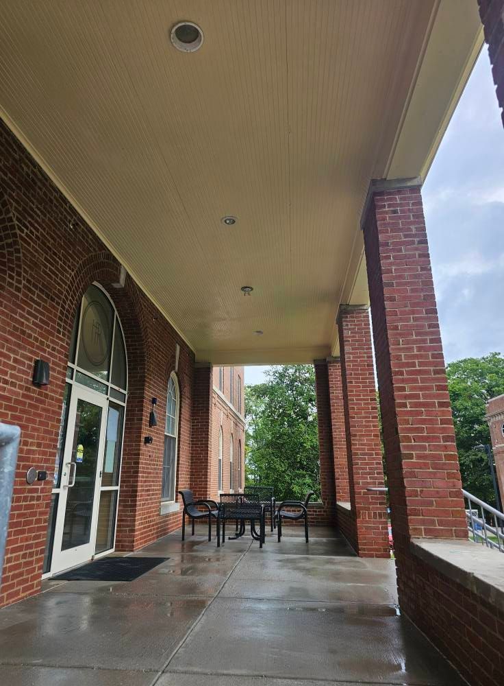 Covered brick porch with white columns, wet concrete floor, and outdoor tables beside a glass door