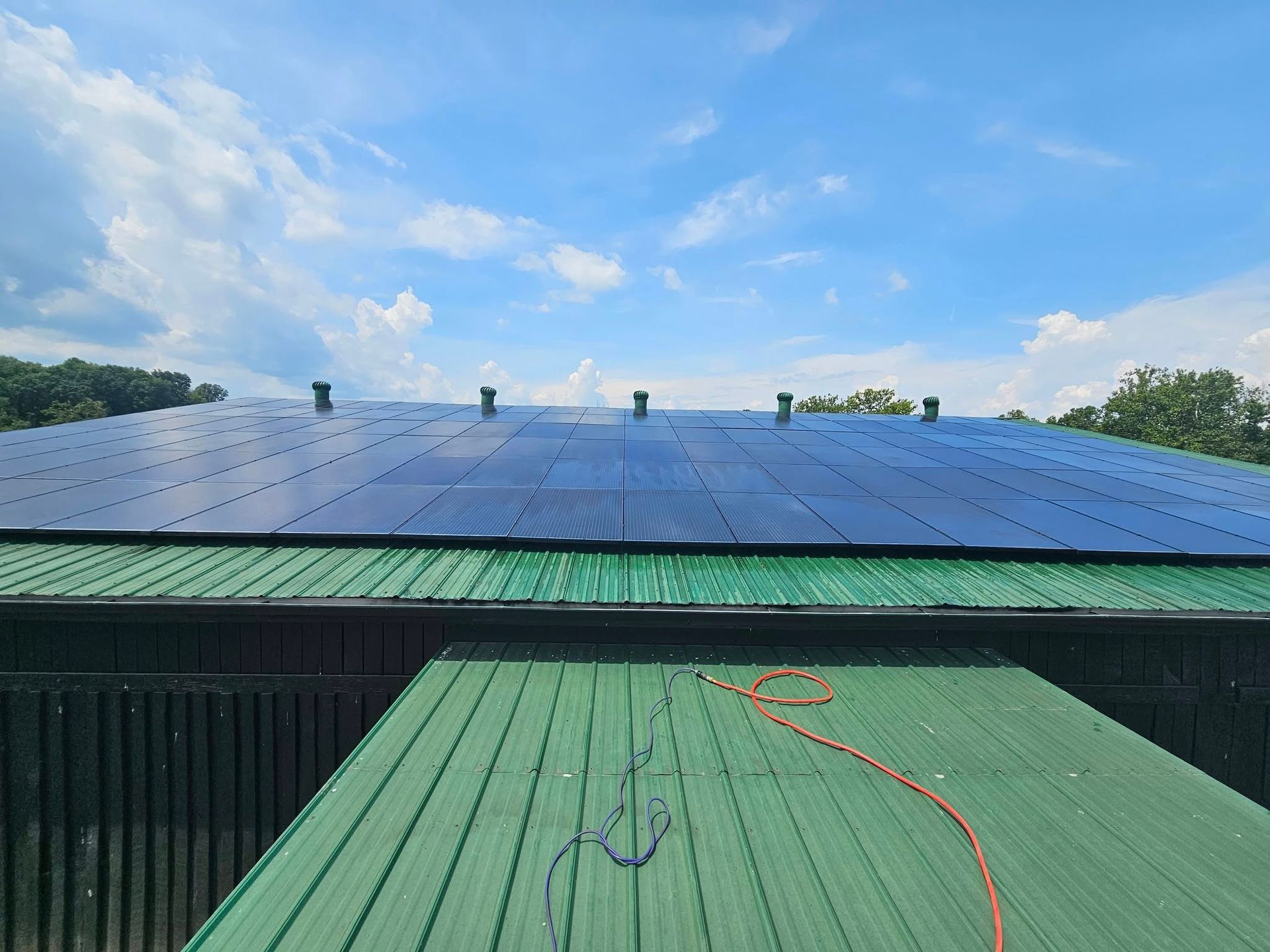 Solar panels on a rooftop with blue sky and clouds above, green roof in the foreground.