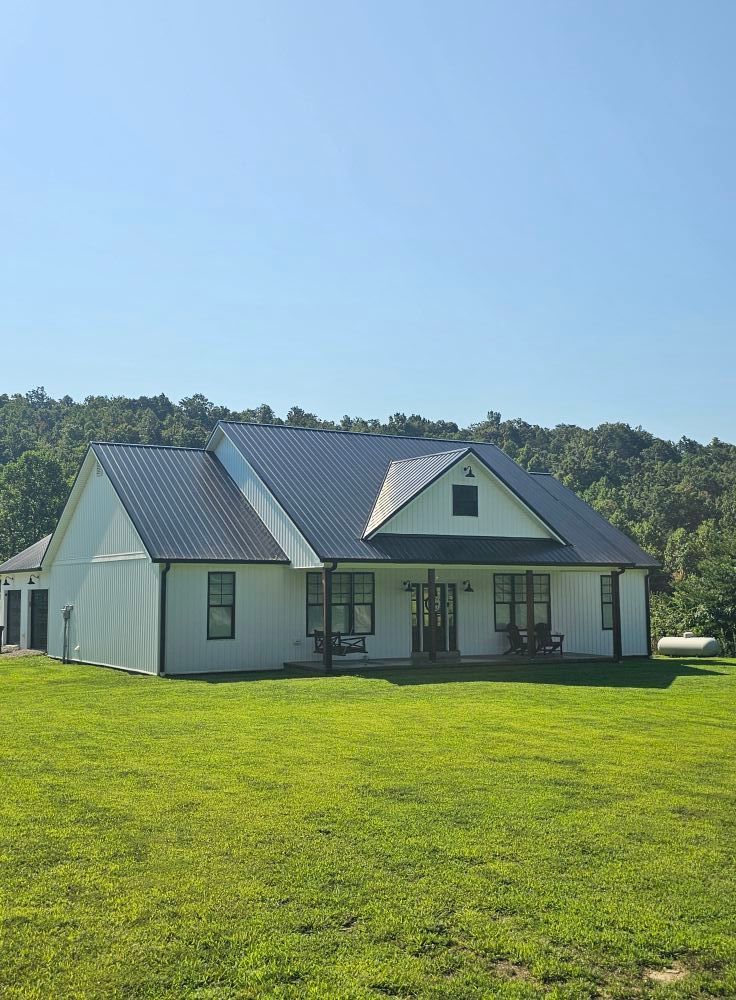 White house with gray roof on a sunny green lawn, backed by trees and blue sky