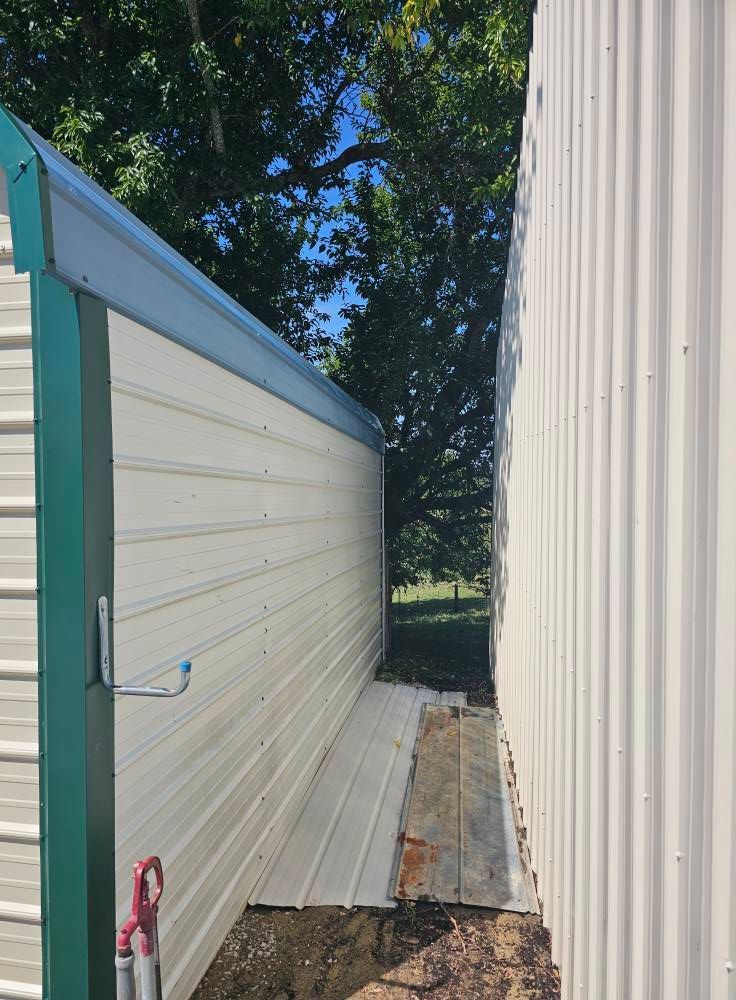 Narrow outdoor passage between two buildings, with a white fence on the left and corrugated metal wall on the right.